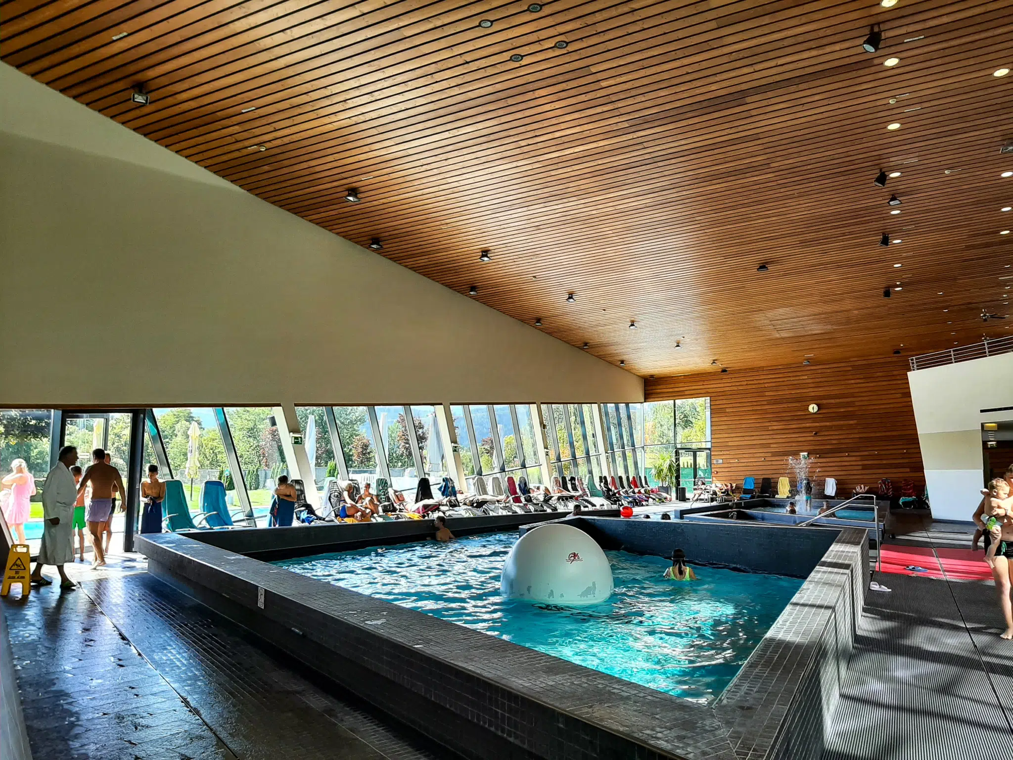 Ihr seht ein Schwimmbecken und die wunderschöne Holzdecke in der Aqualux Therme. JUFA Hotels bietet tollen Urlaub mit viel Abenteuer und Spaß für die ganze Familie.