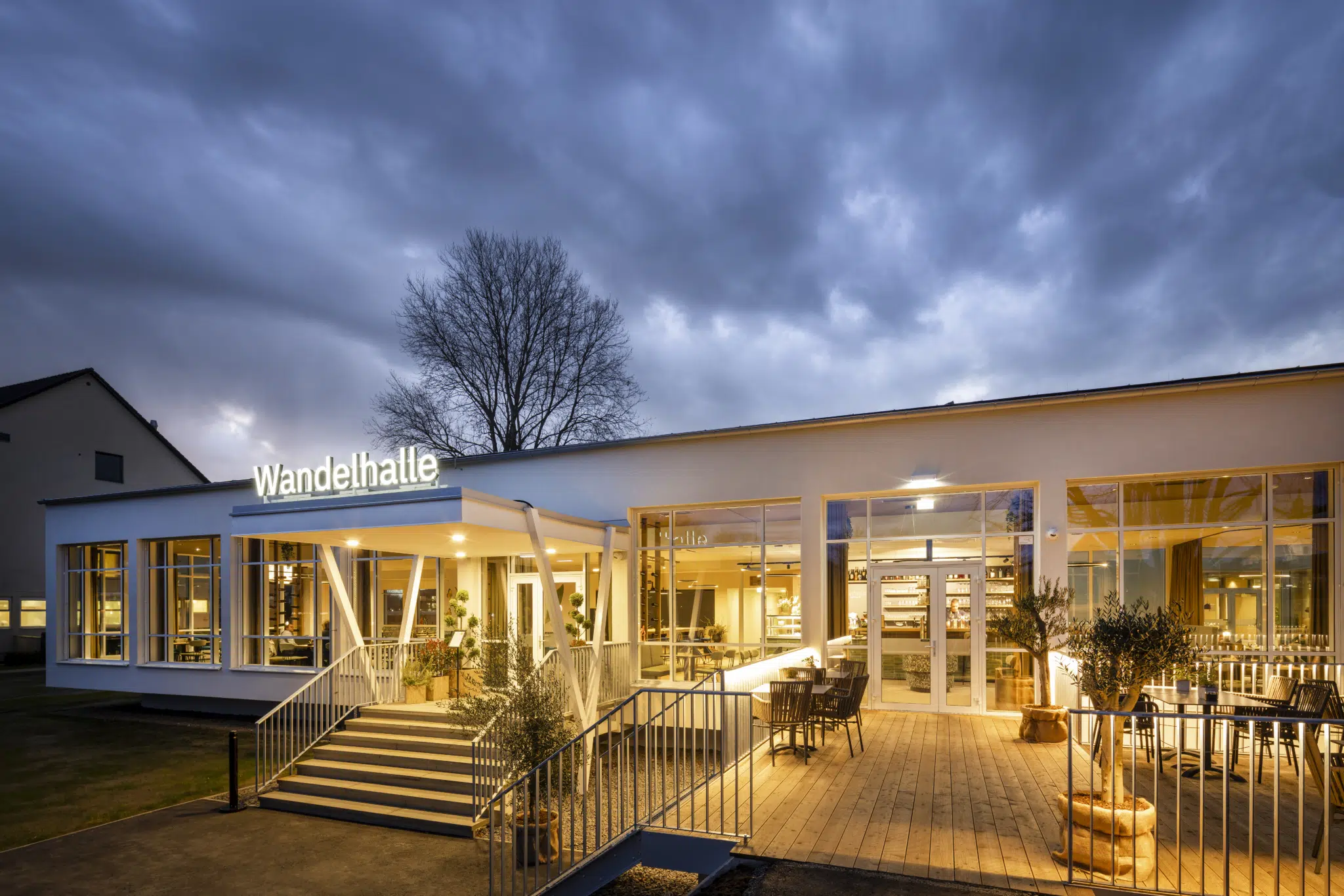 Ihr seht eine Außenansicht in der Abendstimmung des Café & Restaurant Wandelhalle im JUFA Hotel Bad Radkersburg mit großer Terrasse im Kurpark Bad Radkersburg.