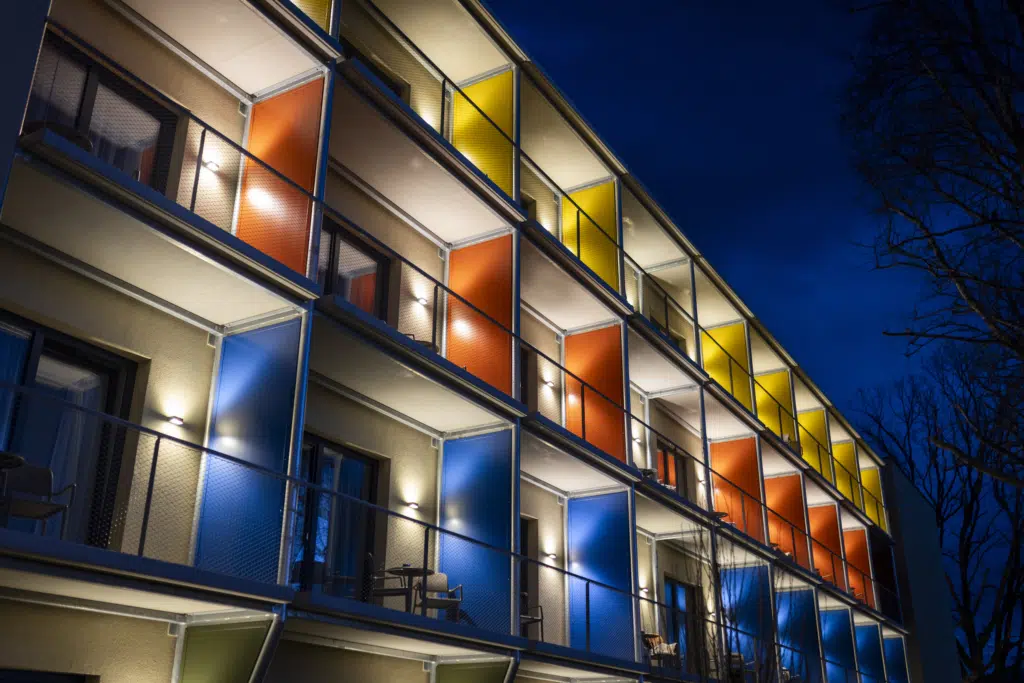 Ihr seht die vollständig beleuchteten Balkone aller Zimmer mit Tische & Sessel im neuen JUFA Hotel Bad Radkersburg in der Nacht.