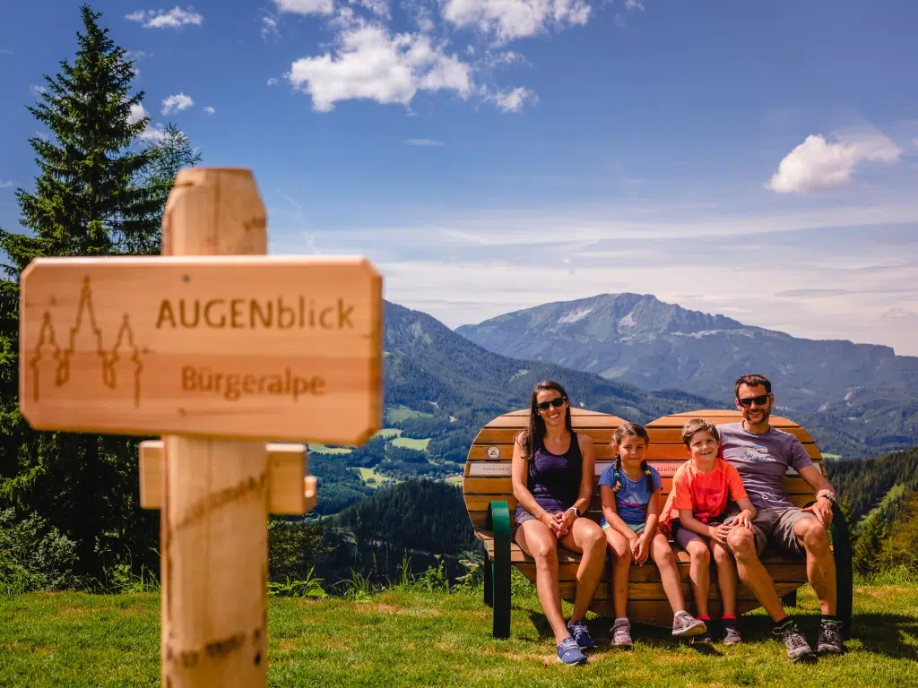 Ihr seht eine Familie auf einer Bank in Herzform sitzend beim Aussichtspunkt Augenblick auf der Bürgeralpe im Mariazeller Land.