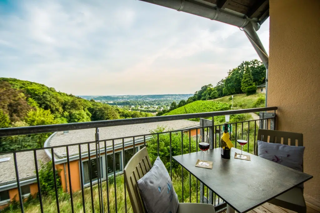 Ihr seht den Balkon eines Zimmers im JUFA Hotel Königswinter**** mit Wein und tollem Ausblick. JUFA Hotels bietet erlebnisreichen Städtetrip für die ganze Familie und den idealen Platz für Ihr Seminar.