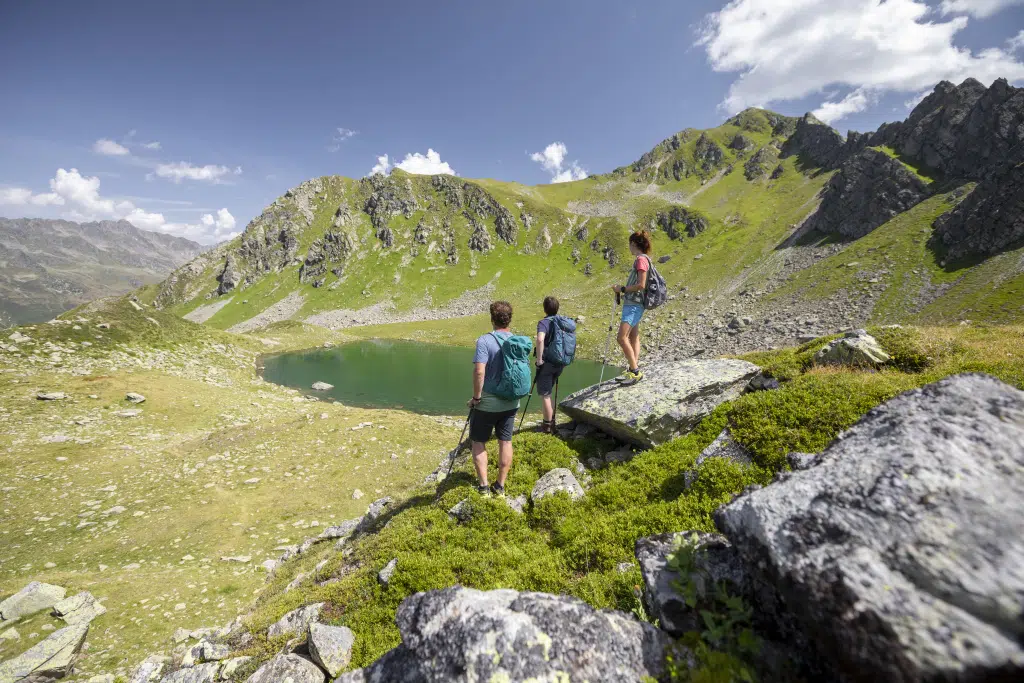 Sie sehen eine Familie, die den Ausblick auf einen Bergsee in den Montafoner Bergen geniesst und eine kurze Rast macht. JUFA Hotels bietet kinderfreundlichen und erlebnisreichen Urlaub für die ganze Familie.