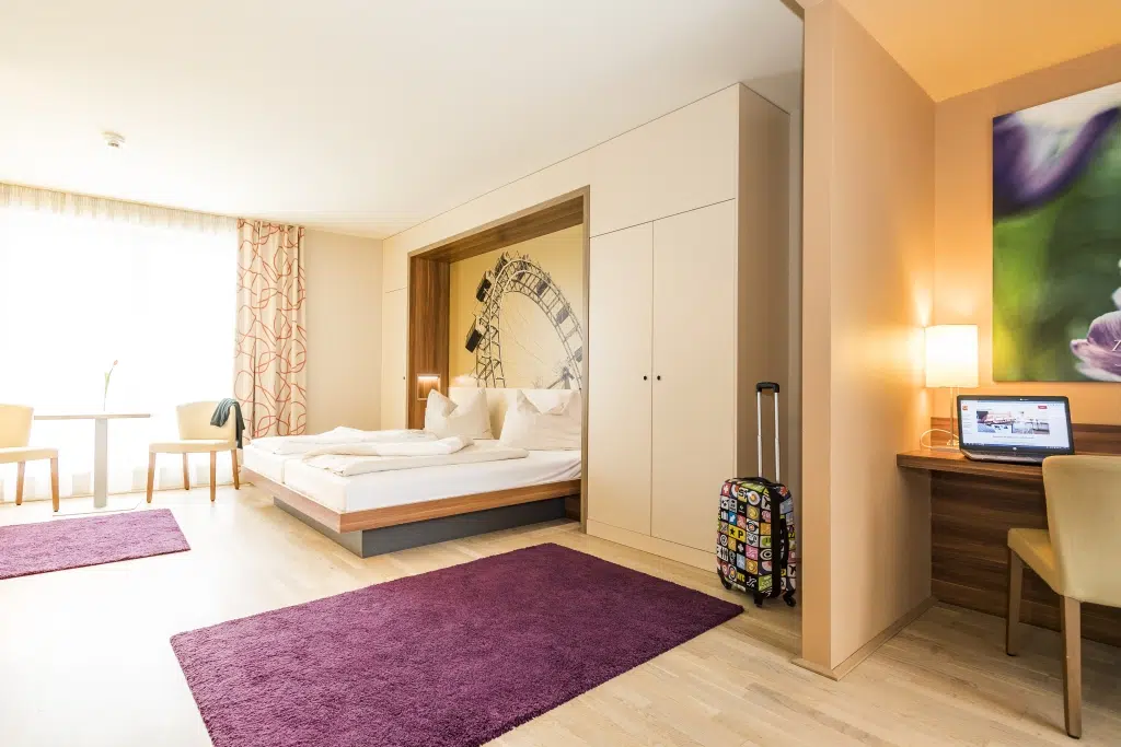 Bett in der Suite large mit Schreibtisch im JUFA Hotel Wien City. Der Ort für erlebnisreichen Städtetrip für die ganze Familie und der ideale Platz für Euer Seminar.