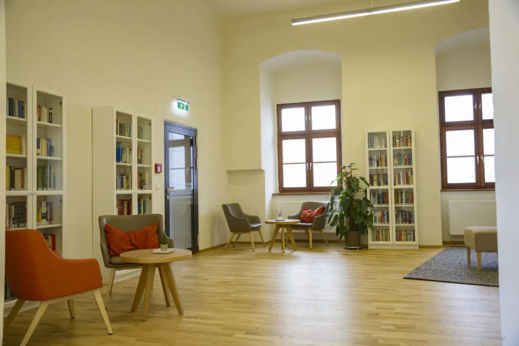 Ihr seht die Bibliothek mit bequemen Sesseln, Bücherregalen und Fenster im JUFA Hotel Spital am Pyhrn***.