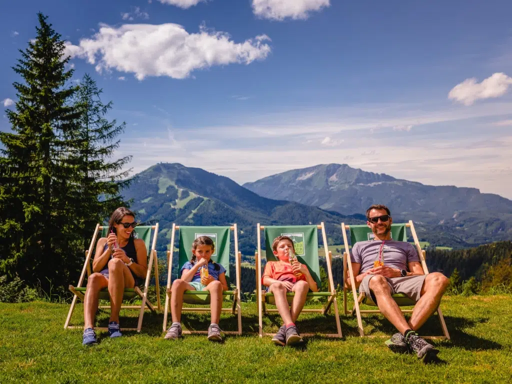 Ihr seht eine 4-köpfige Familie in Liegestühlen und Getränken auf der Bürgeralpe.