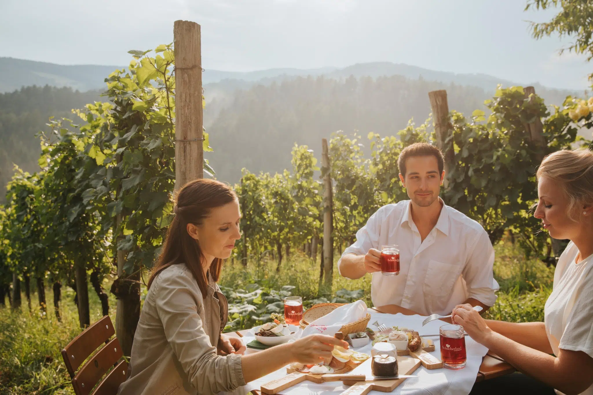 Ihr seht zwei Frauen und ein Mann bei einer Buschenschankjause in der Steiermark. JUFA Hotels bietet Ihnen den Ort für erlebnisreichen Natururlaub für die ganze Familie.