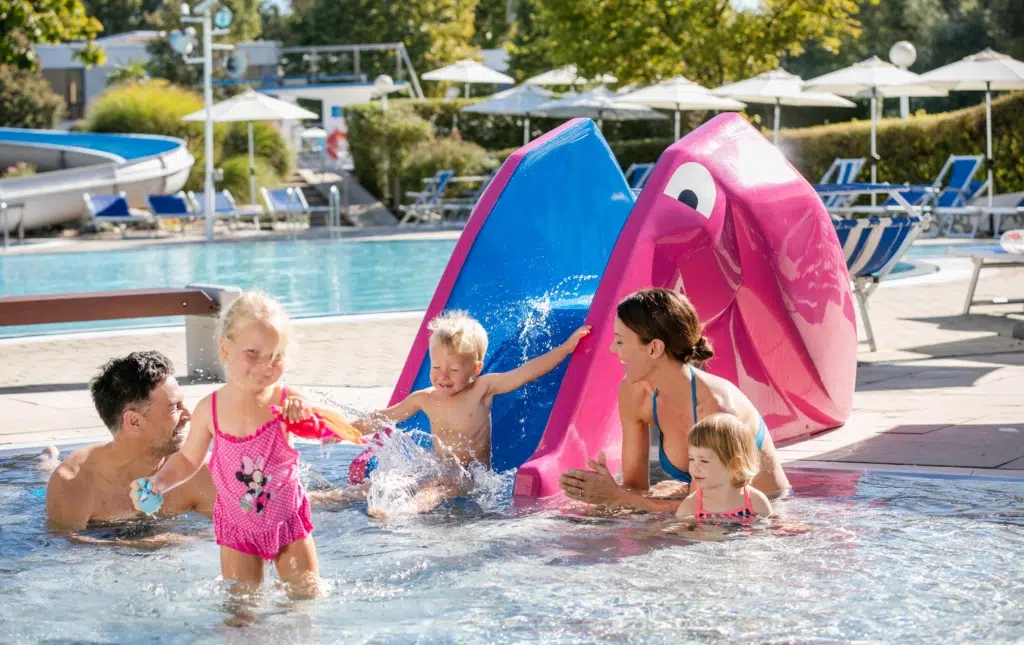 Ihr seht drei Kinder mit ihren beiden Eltern beim Spielen im Wasserspielbereich der Parktherme Bad Radkersburg im Sommer.