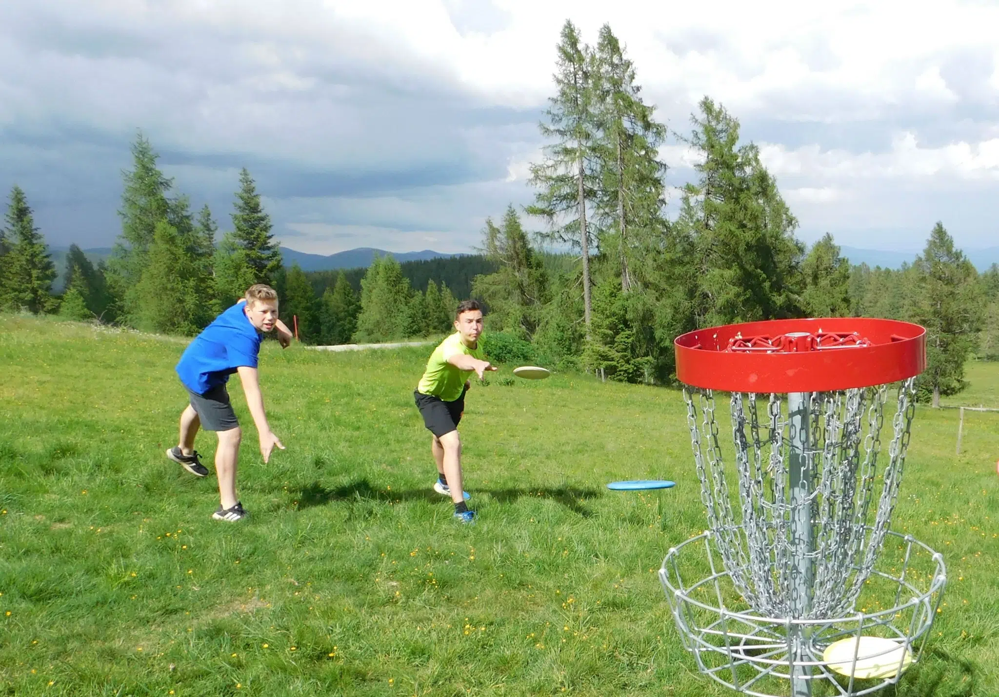 Ihr seht zwei Burschen beim Discgolf-Spielen auf der Hochrindl in der Nähe des JUFA Hotel Nockberge. Der Ort für erholsamen Familienurlaub und einen unvergesslichen Winter- und Wanderurlaub.