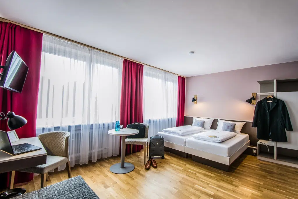 Ihr seht ein Doppelbett in einem Familienzimmer Typ Family and Friends 3 im JUFA Hotel Königswinter**** mit Tisch. JUFA Hotels bietet erlebnisreichen Städtetrip für die ganze Familie und den idealen Platz für Ihr Seminar.