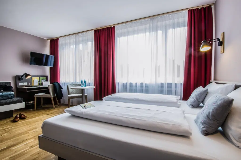 Ihr seht ein Doppelbett in einem Familienzimmer Typ Family and Friends 3 im JUFA Hotel Königswinter**** mit TV. JUFA Hotels bietet erlebnisreichen Städtetrip für die ganze Familie und den idealen Platz für Ihr Seminar.