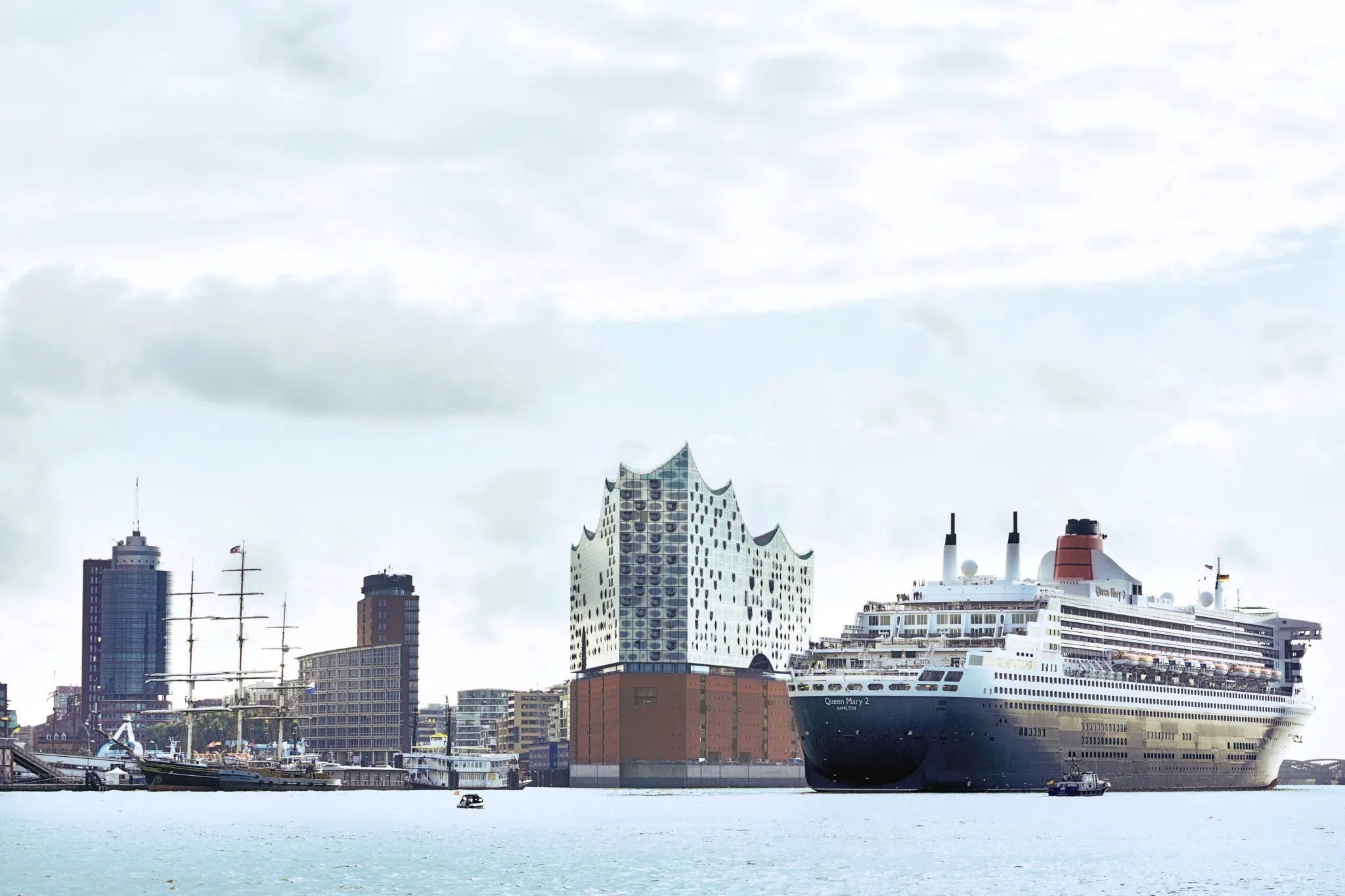 Ihr seht die Queen Mary2 und Elbphilharmonie im Hamburger Hafen im Sommer. JUFA Hotels bietet erlebnisreichen Städtetrip für die ganze Familie und den idealen Platz für Ihr Seminar.