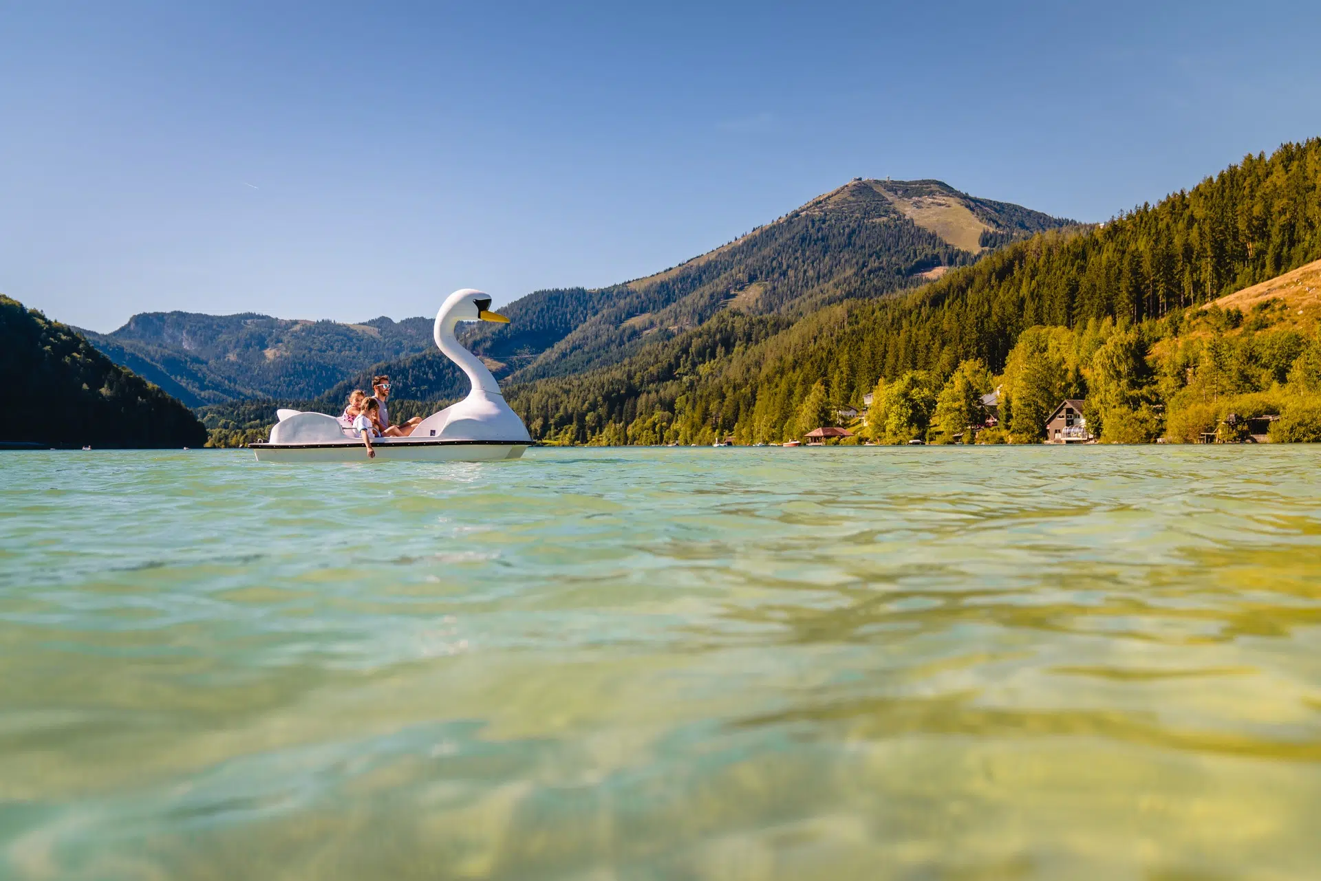 Ihr seht den Erlaufsee im Mariazellerland mit einem Tretboot, mit dem eine Familie über den See fährt, zwischen der Steiermark und Niederösterreich. JUFA Hotels bietet Ihnen den Ort für erlebnisreichen Natururlaub für die ganze Familie.