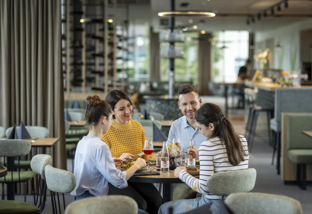 Ihr seht eine vierköpfige Familie beim gemütlichen Mittag- und Abendessen im Café & Restaurant Wandelhalle im JUFA Hotel Bad Radkersburg****