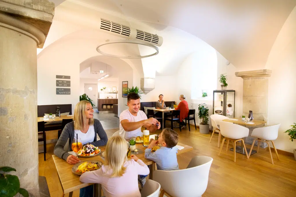 Ihr seht eine Familie beim Essen im Restaurant des JUFA Hotel Festung Rosenberg Kronach***s. Der Ort für kinderfreundlichen und erlebnisreichen Urlaub für die ganze Familie.