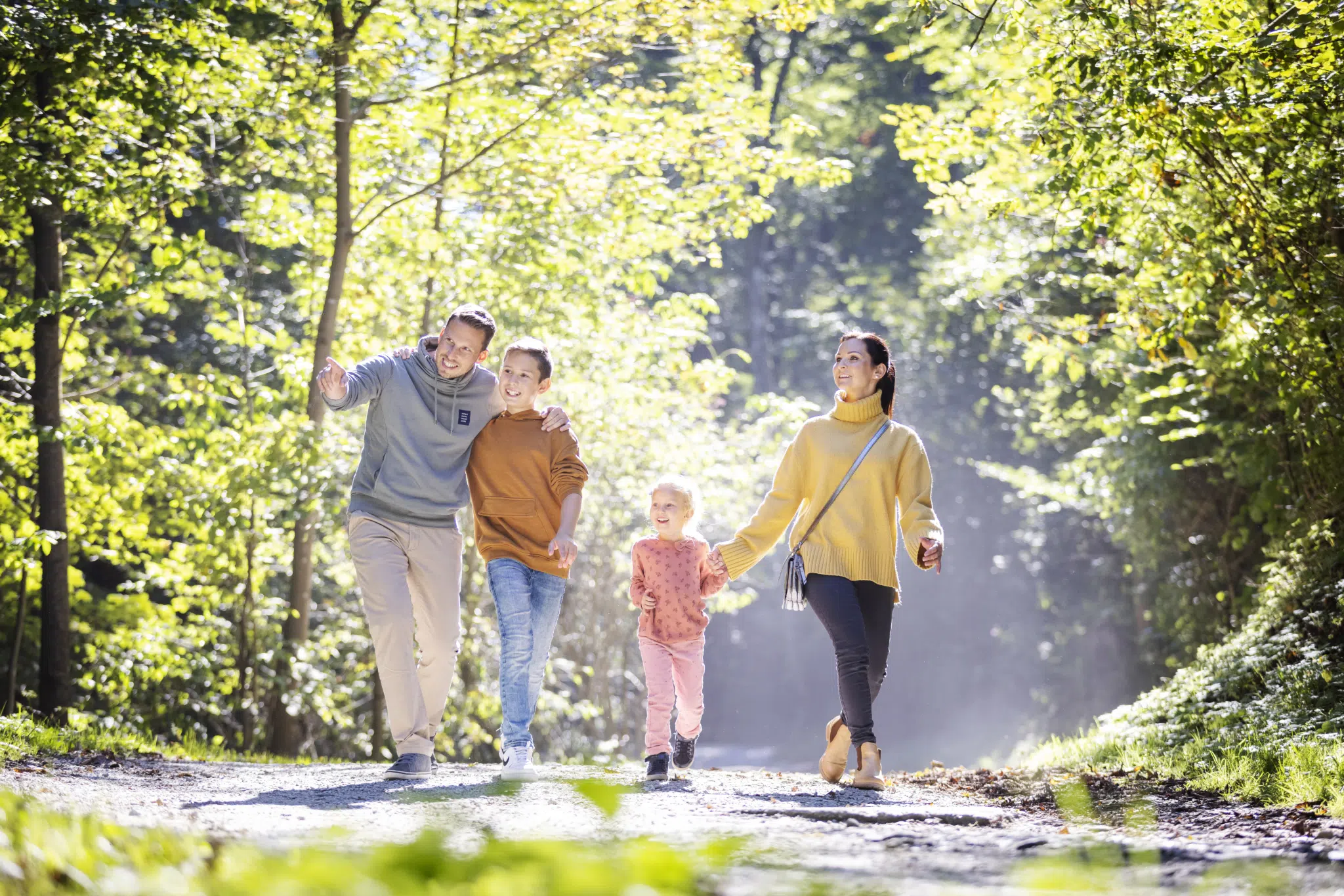 Ihr seht eine Familie bei einem Herbstspaziergang mit Sonnenstrahlen. Der Papa zeigt in die Ferne und hat einen Arm um seinen Sohn gelegt. JUFA Hotels bietet erholsamen Familienurlaub und einen unvergesslichen Winter- und Wanderurlaub.