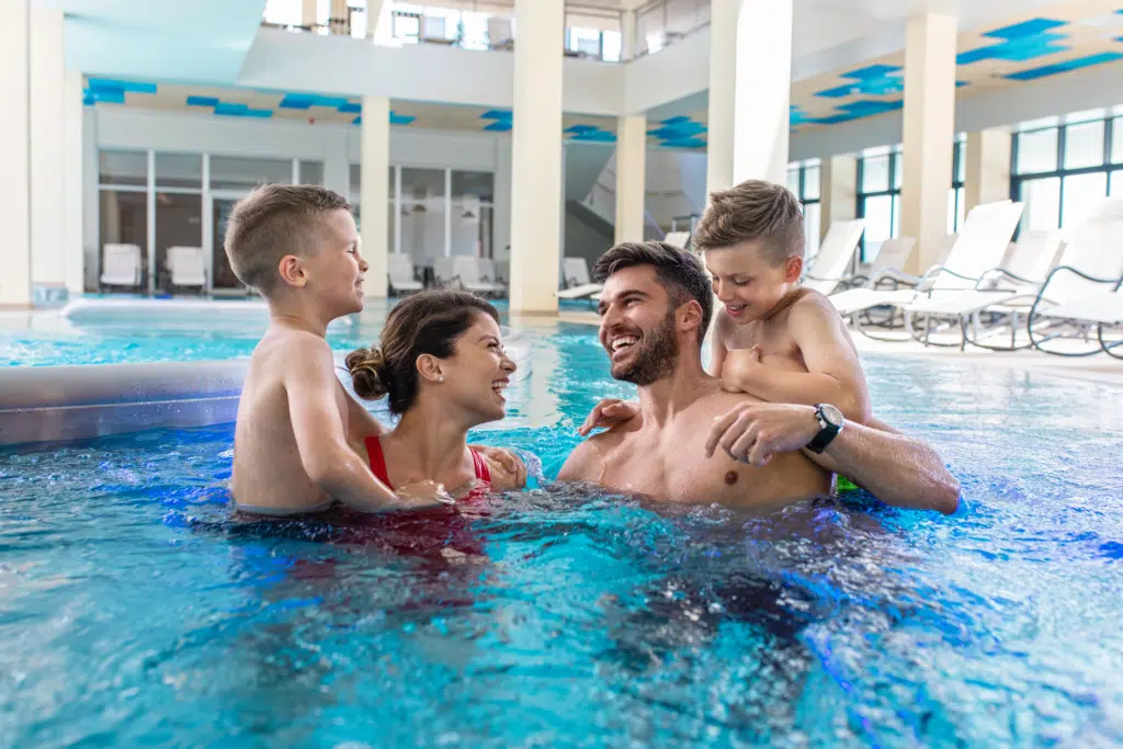 Ihr seht eine Familie mit Kindern beim Baden und Entspannen im Innenbereich einer Therme in der Nähe von JUFA Hotels.