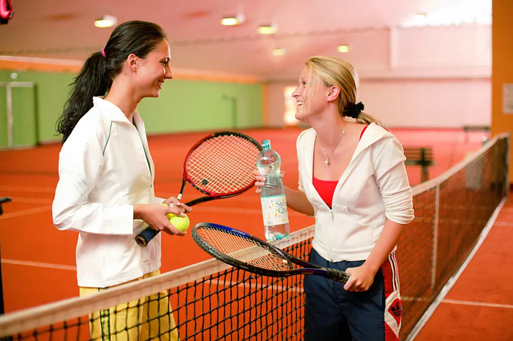 Ihr seht zwei Frauen beim Tennis in der Tennishalle des JUFA Hotel Vulkanland – Sport-Resort. Der Ort für erfolgreiches Training in ungezwungener Atmosphäre für Vereine und Teams.