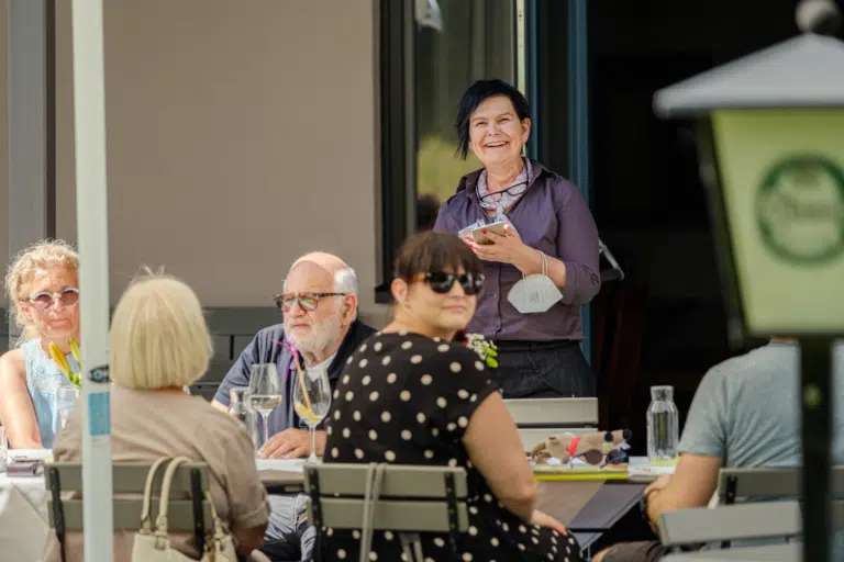 Ihr seht Gäste im Gastgarten beim Bestellen von Speisen und Getränke. JUFA Hotels bietet kinderfreundlichen und erlebnisreichen Urlaub für die ganze Familie.