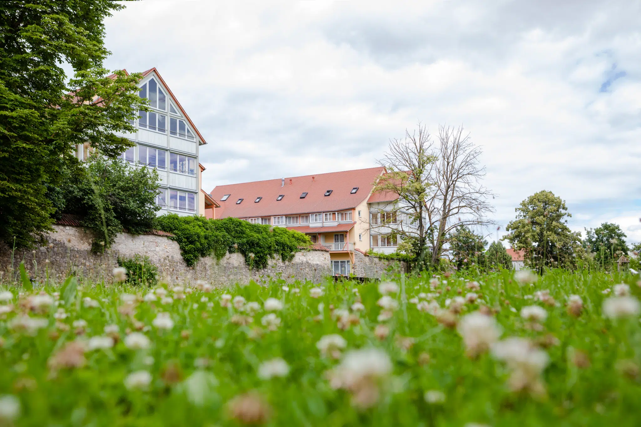 Ihr seht die Hausansicht im Sommer mit grüner Wiese vom JUFA Hotel Nördlingen***. Der Ort für kinderfreundlichen und erlebnisreichen Urlaub für die ganze Familie.