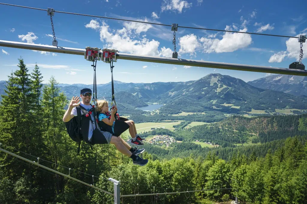 Ihr seht einen Vater mit seinem Kind beim Flying Fox mit einer schönen Naturkulisse im Hintergrund.