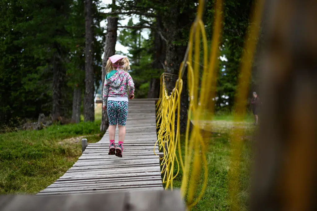 Ihr seht ein Mädchen auf einer Holzsprungmatte beim Zirbenzapfis Erlebnisweg. JUFA Hotels bietet erholsamen Ski- und Wanderurlaub für Familien in Kärnten.