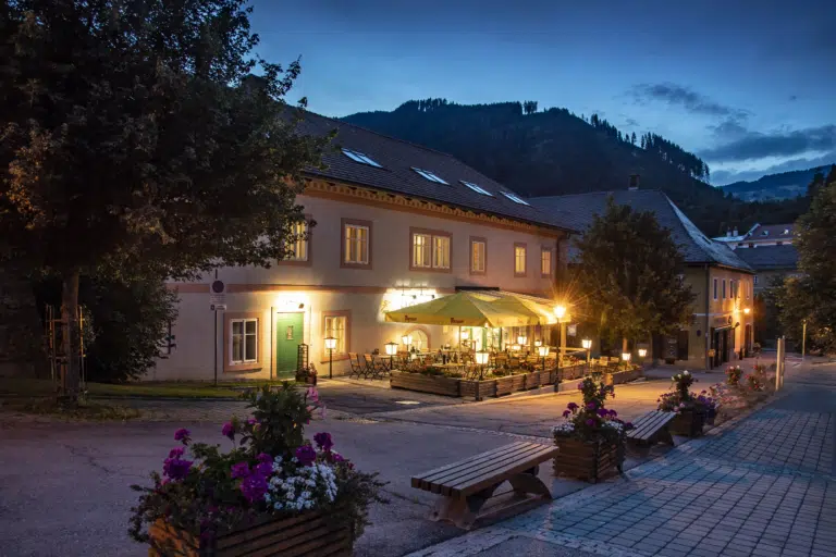 Ihr seht eine Außenansicht mit Gastgarten vom JUFA Hotel Murau am Abend. JUFA Hotels bietet erholsamen Familienurlaub und einen unvergesslichen Winter- und Wanderurlaub.