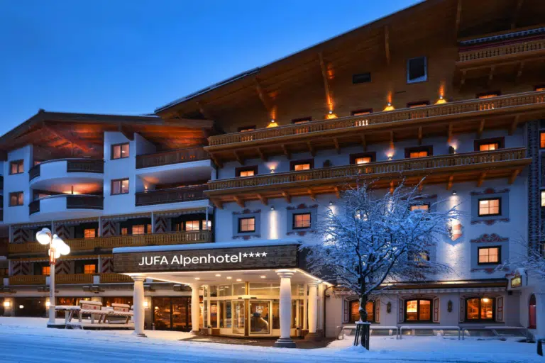 Ihr seht die Außenansicht vom JUFA Alpenhotel Saalbach**** am Abend im Winter.