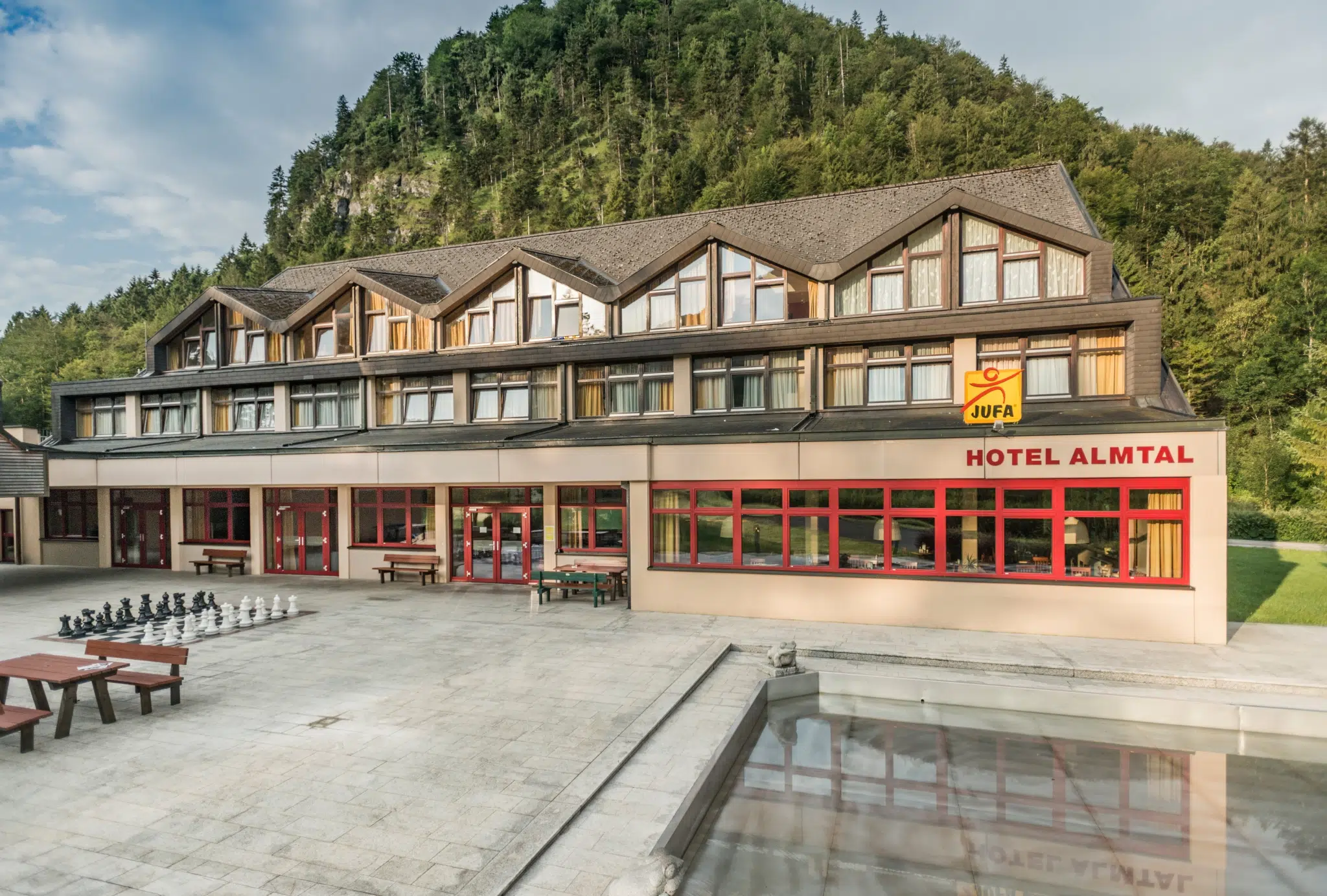 Außenansicht vom JUFA Hotel Grünau im Almtal mit Terrasse im Sommer. JUFA Hotels bieten erholsamen Familienurlaub und einen unvergesslichen Winter- und Wanderurlaub.