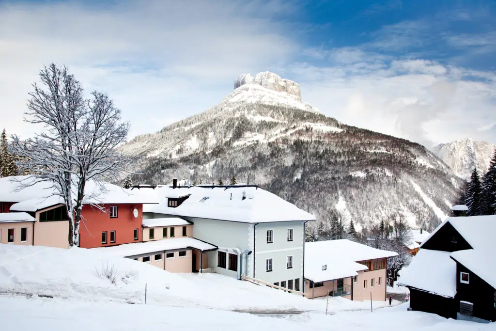 Ihr seht eine Außenansicht vom JUFA Hotel Altaussee*** mit Loser im Winter. JUFA Hotels bietet erholsamen Familienurlaub und einen unvergesslichen Winterurlaub.