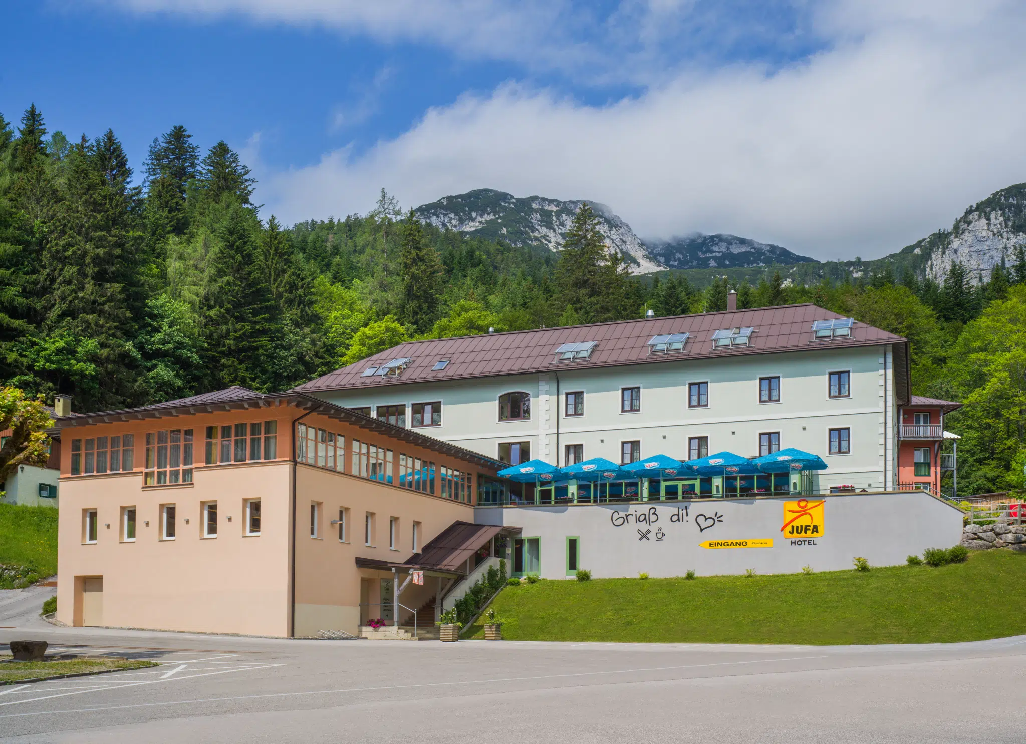 Ihr seht die Hotelansicht im Sommer mit grünen Bäumen und Sträuchern vom JUFA Hotel Altaussee***. Der Ort für erlebnisreichen Natururlaub für die ganze Familie.