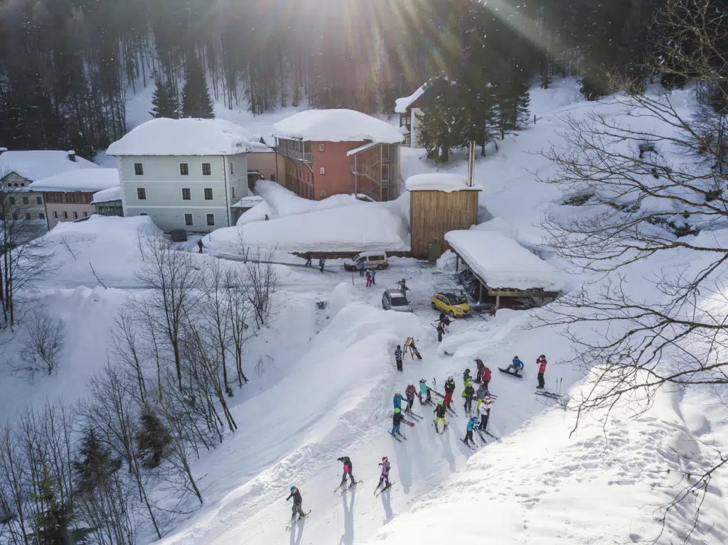 Ihr seht eine Außenansicht vom JUFA Hotel Altaussee*** mit einer Skigruppe im Winter. JUFA Hotels bietet erholsamen Familienurlaub und einen unvergesslichen Winterurlaub.