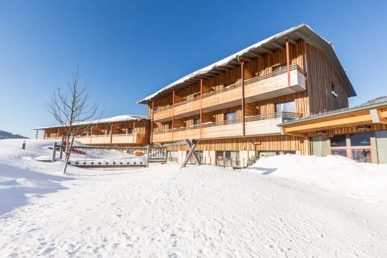 Ihr seht die Aussenansicht vom JUFA Hotel Annaberg***s vor blauem Himmel im Winter. Der Ort für erholsamen Familienurlaub und einen unvergesslichen Winter- und Wanderurlaub.