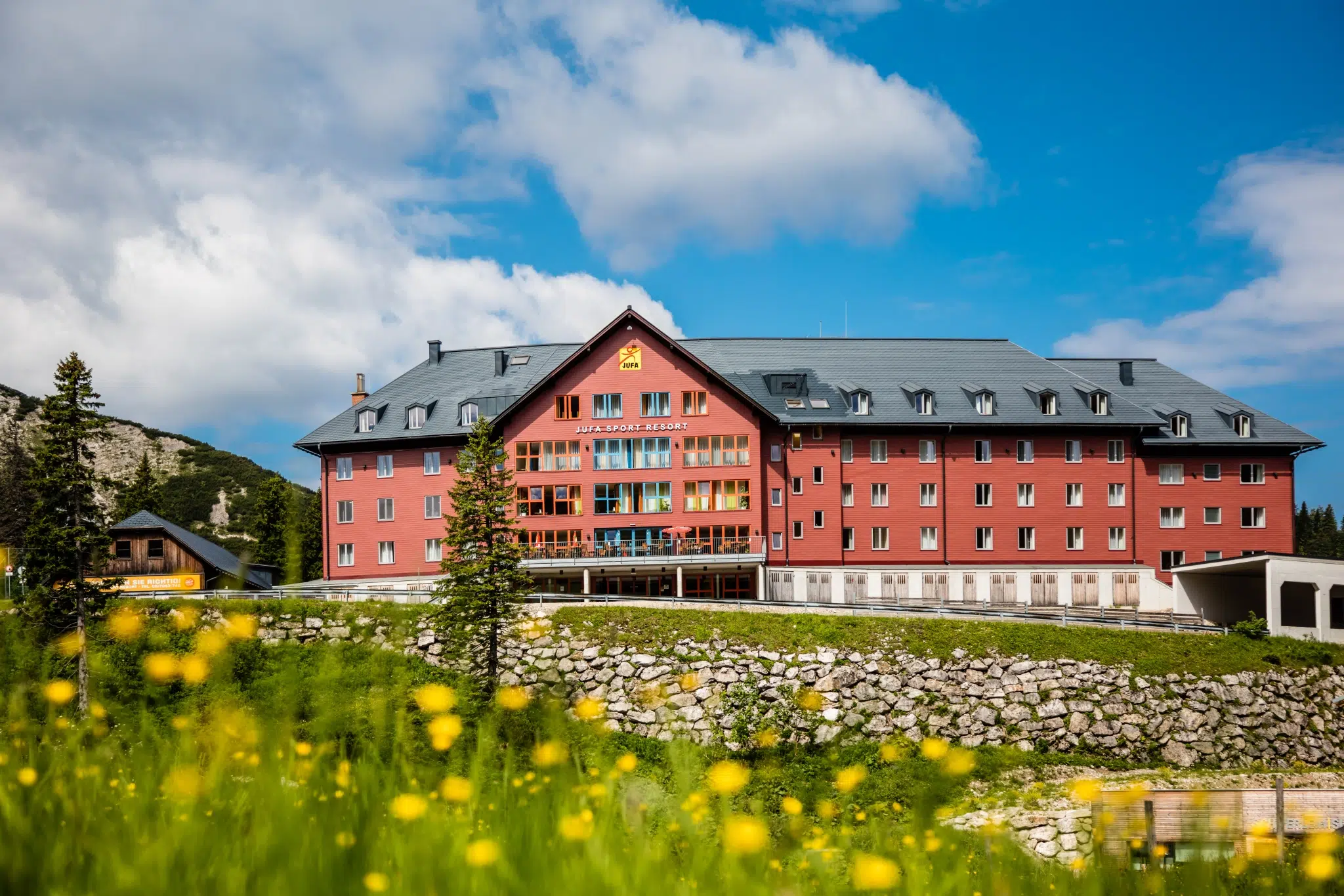 Frontale Hotelansicht mit blühender Wiese im Sommer vom JUFA Hotel Hochkar Sport-Resort. Der Ort für erfolgreiches Training in ungezwungener Atmosphäre für Vereine und Teams.