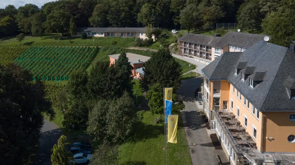 Ihr seht eine Außenansicht vom JUFA Hotel Königswinter**** mit einem Weinberg im Sommer. JUFA Hotels bietet erlebnisreichen Städtetrip für die ganze Familie und den idealen Platz für Ihr Seminar.