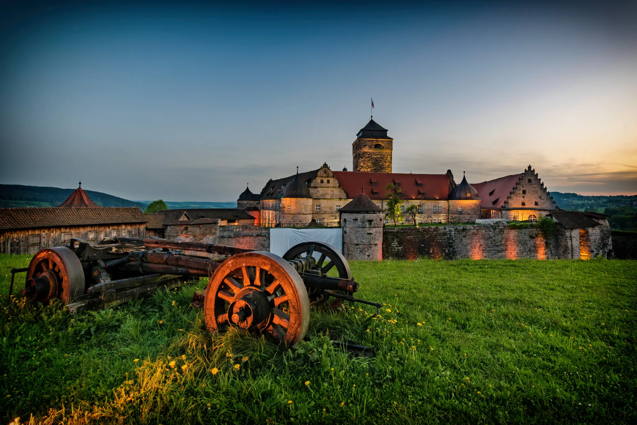 Ihr seht eine Außenansicht vom JUFA Hotel Festung Rosenberg Kronach***s bei Abenddämmerung im Sommer. JUFA Hotels bietet kinderfreundlichen und erlebnisreichen Urlaub für die ganze Familie.