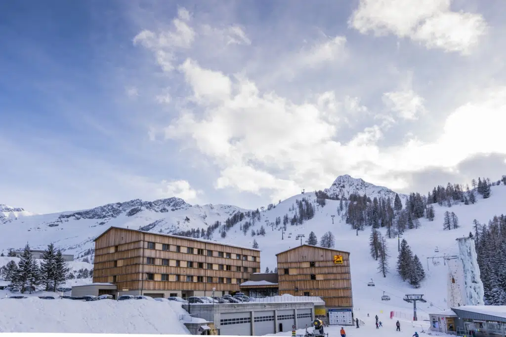 Sie sehen eine Außenansicht vom JUFA Hotel Malbun – Alpin-Resort*** mit Piste im Winter. JUFA Hotels bietet erholsamen Familienurlaub und einen unvergesslichen Winterurlaub.