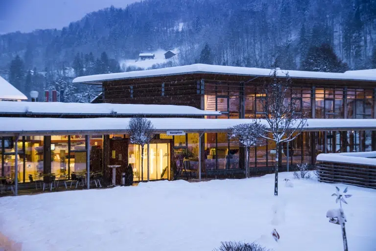 Aussenansicht mit Eingang im Winter vom JUFA Hotel Montafon in der Abenddämmerung. Der Ort für erholsamen Familienurlaub und einen unvergesslichen Winter- und Wanderurlaub.