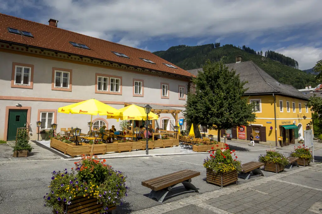 Ihr seht eine Außenansicht vom JUFA Hotel Murau mit Gastgarten im Sommer. JUFA Hotels bietet erholsamen Familienurlaub und einen unvergesslichen Winter- und Wanderurlaub.