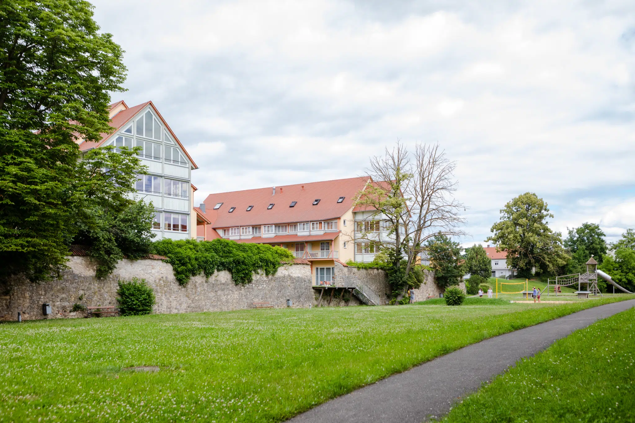 Ihr seht die Hausansicht im Sommer mit grüner Wiese vom JUFA Hotel Nördlingen. Der Ort für kinderfreundlichen und erlebnisreichen Urlaub für die ganze Familie.