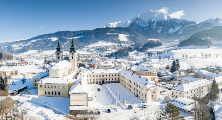 Ihr seht eine Außenansicht vom JUFA Hotel Spital am Pyhrn*** mit Bergen im Winter.