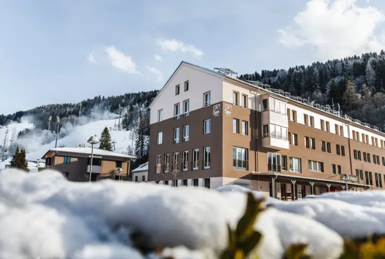 Ihr seht eine Außenansicht vom JUFA Hotel Schladming*** mit Schnee im Winter.