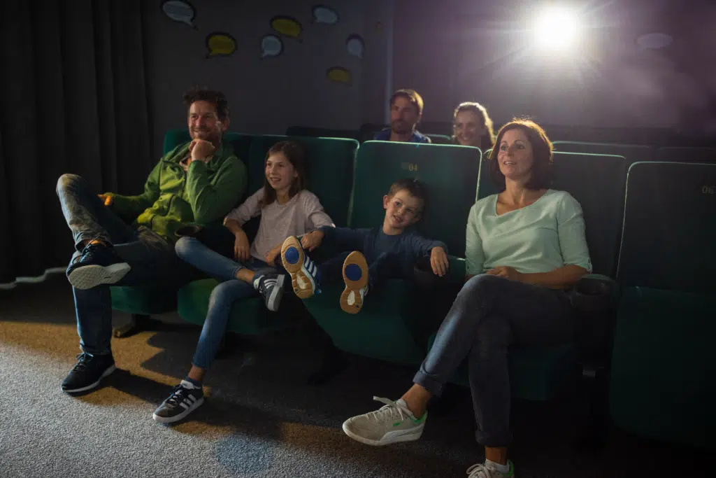 Ihr seht eine Familie im hoteleigenen Kino im JUFA Familienresort Kempten***s. Der Ort für kinderfreundlichen und erlebnisreichen Urlaub für die ganze Familie.