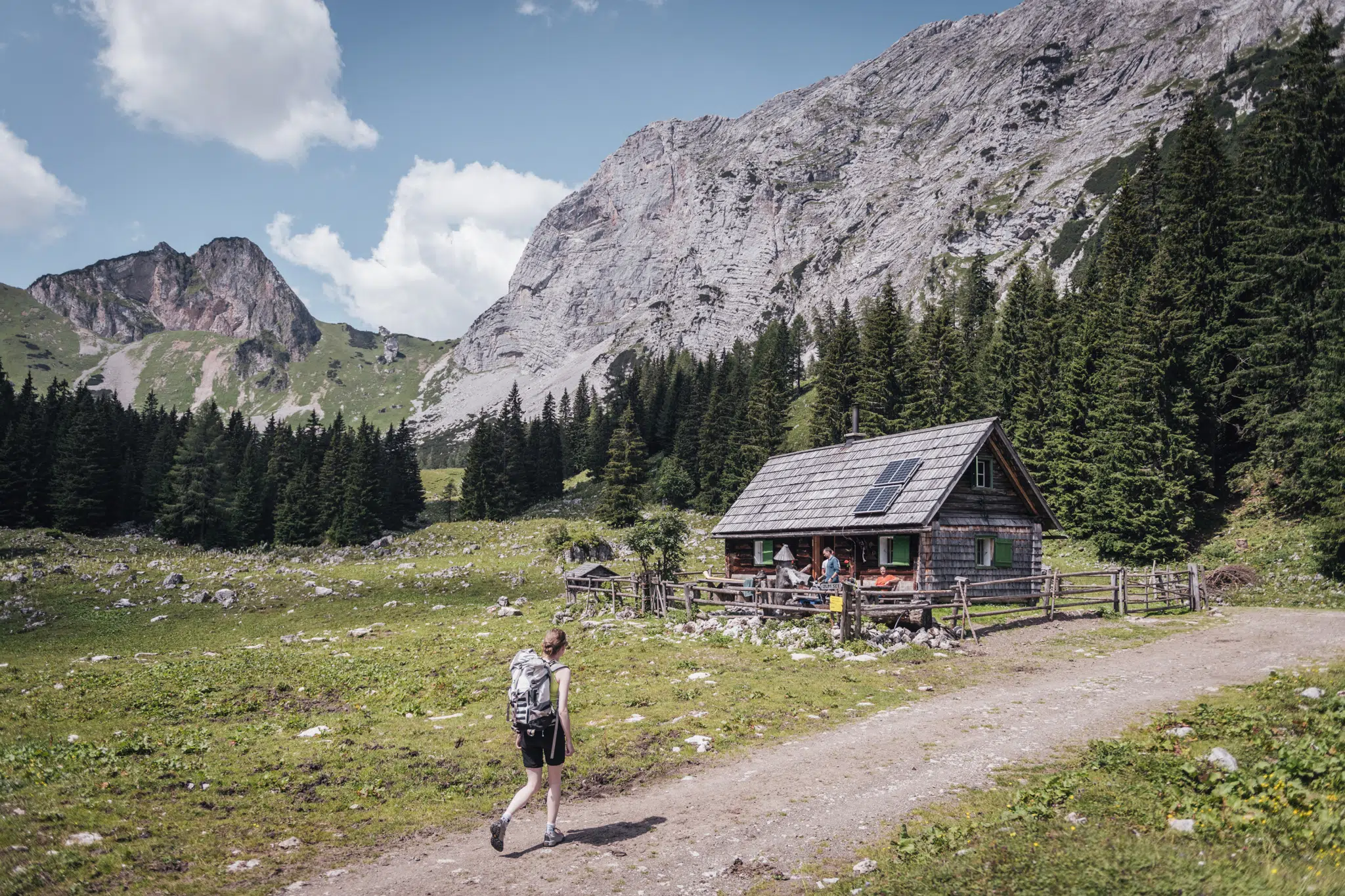 Ihr seht eine Frau, die bei einer Hütte auf der Sulzkaralm im Gesäuse einkehrt. JUFA Hotels bietet euch den Ort für erlebnisreichen Natururlaub für die ganze Familie.