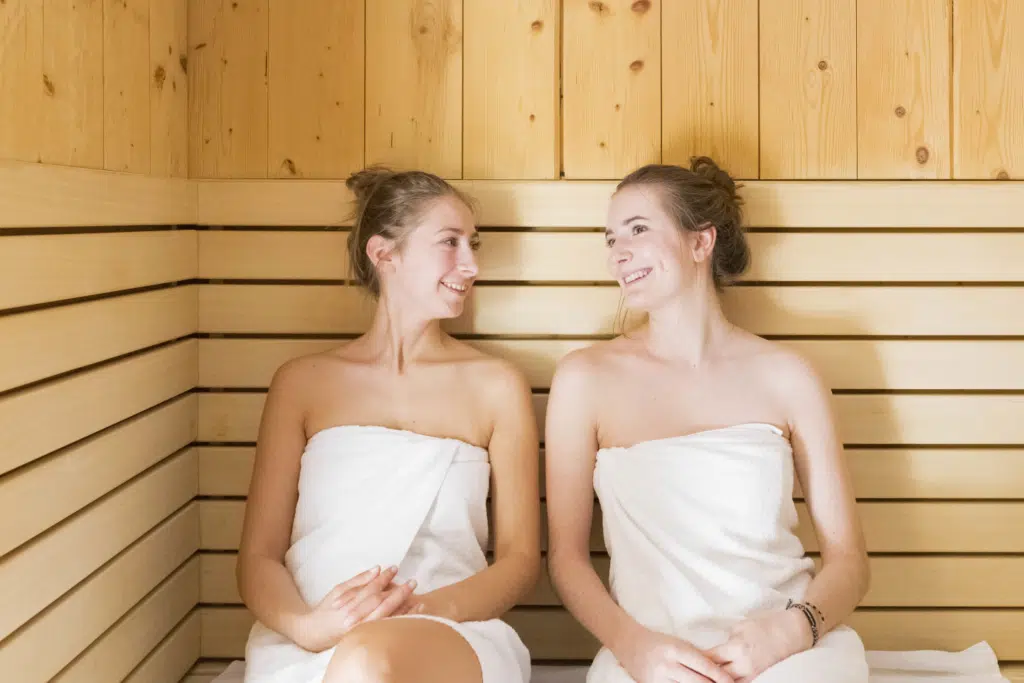 Ihr seht zwei Frauen in der Sauna sitzen mit ihren Saunahandtüchern.