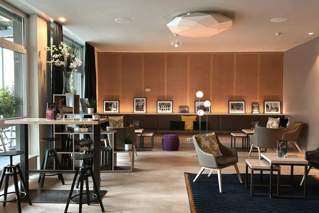 Ihr seht die Lounge des JUFA Hotel Graz City, ausgestattet mit gemütlichen Lehnsesseln, Cafetischen, Holzvertäfelung und gemütlichen Kissen. Der Ort für einen erlebnisreichen Städtetrip für die ganze Familie und der ideale Platz für euer Seminar.