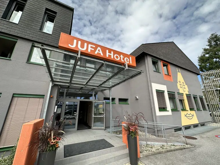 Ihr seht eine Außenansicht des JUFA Hotel Graz Süd mit dem barrierefreien Eingang. Der Ort für erlebnisreichen Städtetrip für die ganze Familie und der ideale Platz für euer Seminar.