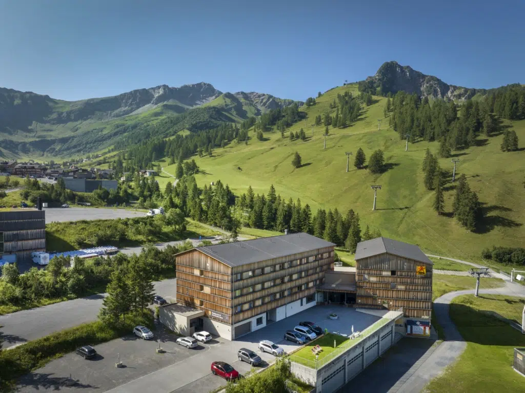 Ihr seht die Aussenansicht des JUFA Hotels Malbun mit dem Bergmassiv im Hintergrund