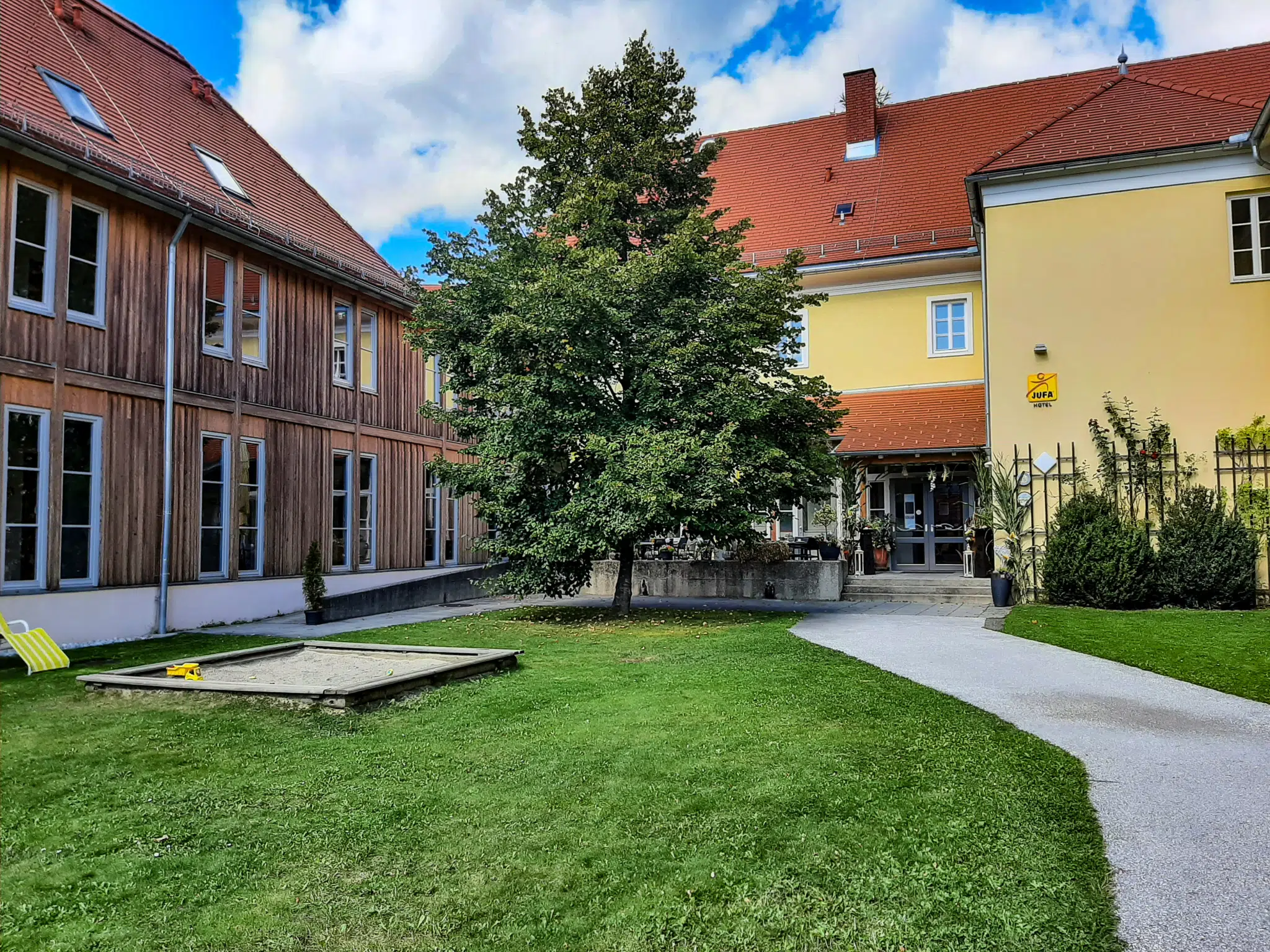 Ihr seht den Eingang zum JUFA Hotel Seckau mit Garten. JUFA Hotels bietet erholsamen Familienurlaub und einen unvergesslichen Winter- und Wanderurlaub.