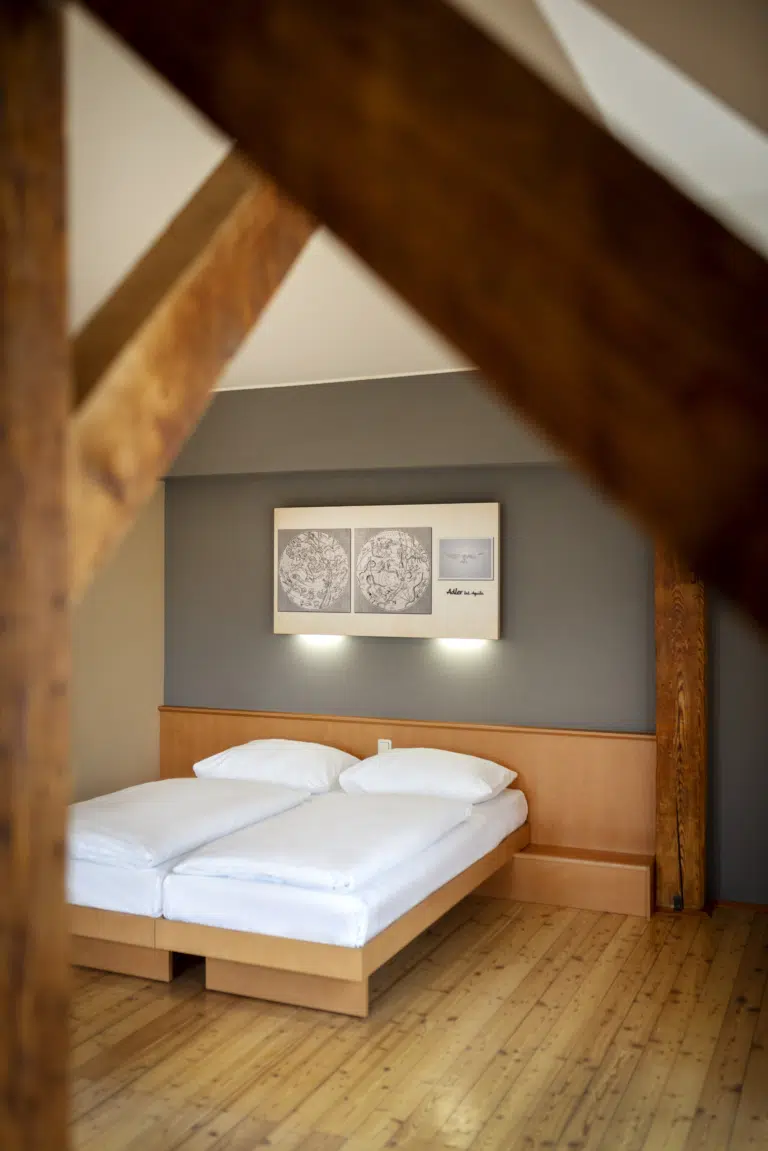 Ihr seht ein Doppelbett. So sind die Doppelzimmer und Einzelzimmer im JUFA Klosterhotel Judenburg ausgestattet. Der Ort für erholsamen Familienurlaub und einen unvergesslichen Winter- und Wanderurlaub.