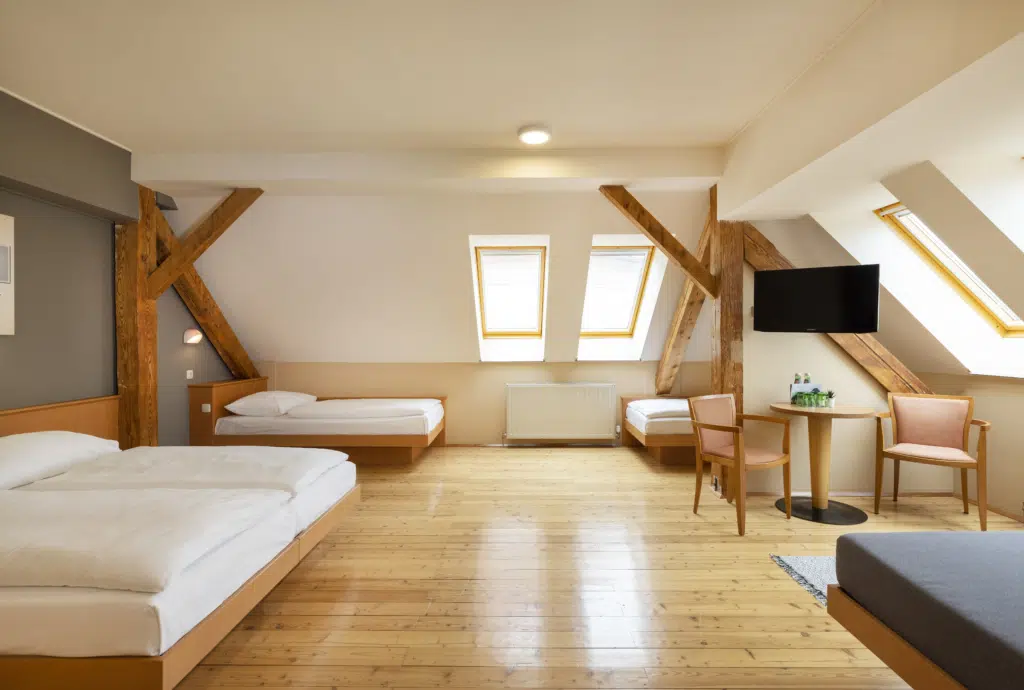 Ihr seht ein Doppelbett und drei Einzelbetten. So sind die Family Friends 5 Zimmer im JUFA Klosterhotel Judenburg ausgestattet. Der Ort für erholsamen Familienurlaub und einen unvergesslichen Winter- und Wanderurlaub.